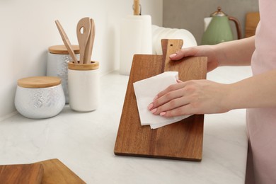 Woman wiping wooden cutting board with paper napkin at white table, closeup