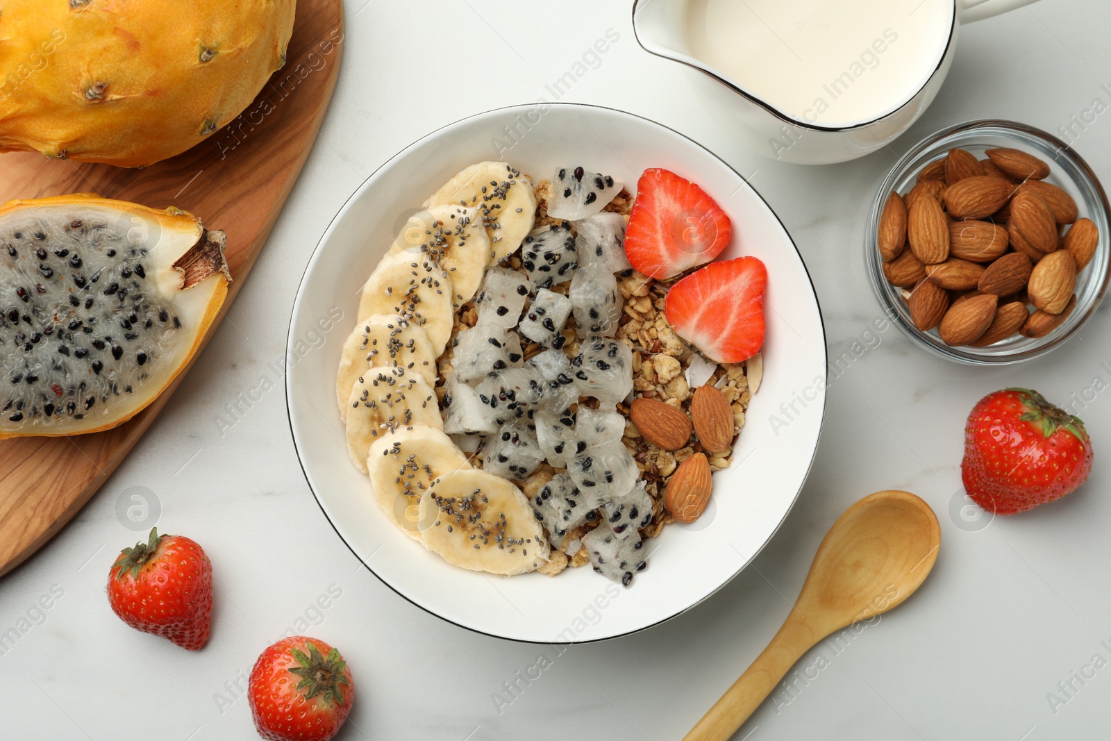 Photo of Bowl of granola with pitahaya, banana and strawberry on white marble table, top view