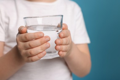 Little boy holding glass of fresh water on light blue background, closeup. Space for text