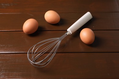 Photo of Metal whisk and raw eggs on wooden table