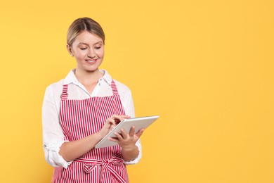 Beautiful young woman in clean striped apron with tablet on orange background. Space for text