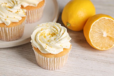 Delicious cupcakes with white cream, lemon zest and lemons on light wooden table, closeup