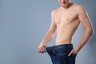 Photo of Young man with slim body in old big size jeans on grey background, closeup. Space for text