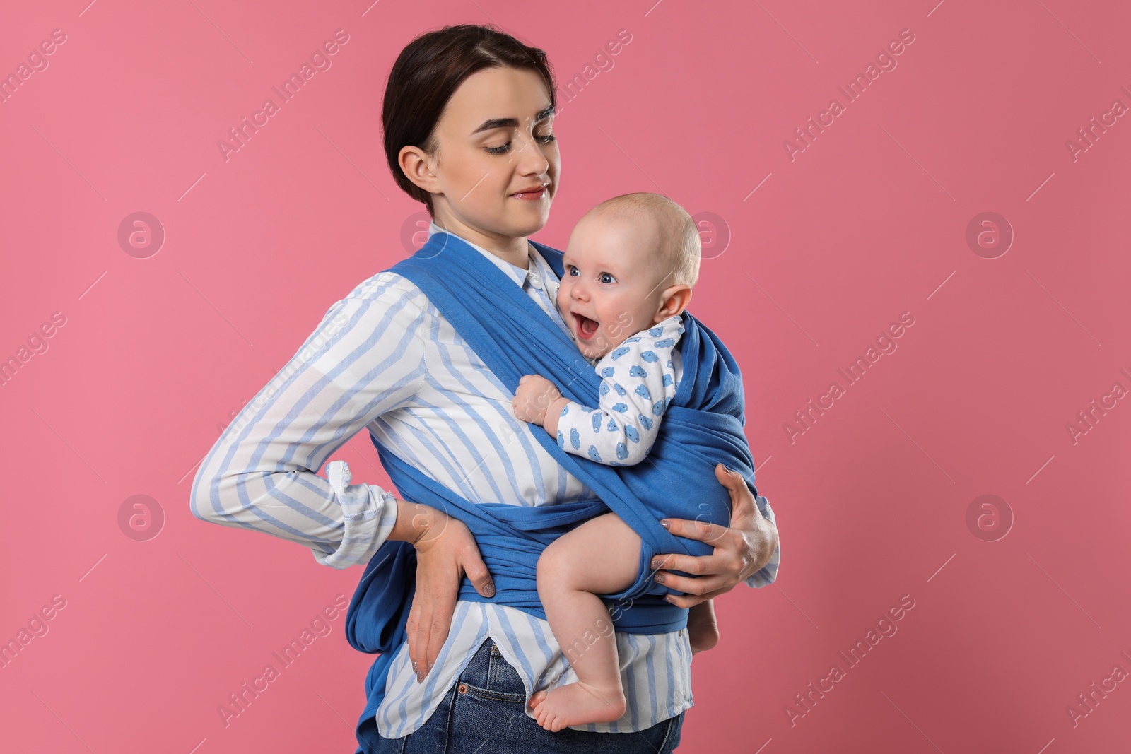 Photo of Mother holding her child in sling (baby carrier) on pink background