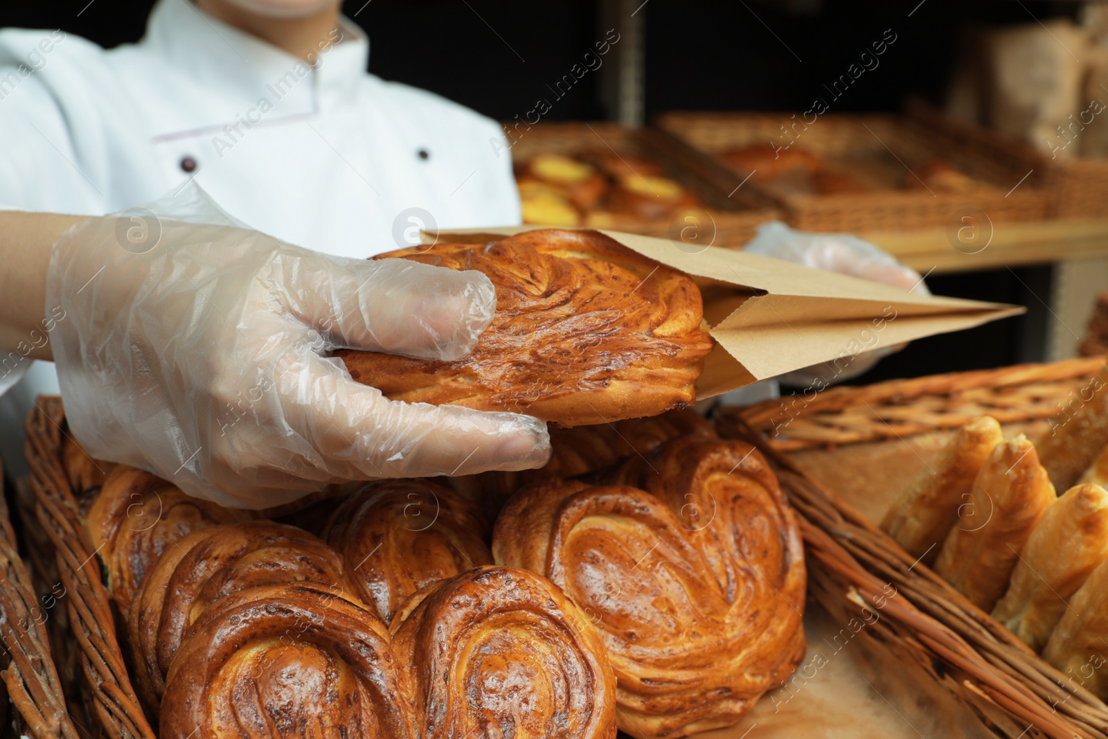 Photo of Baker putting fresh bun into paper bag, closeup