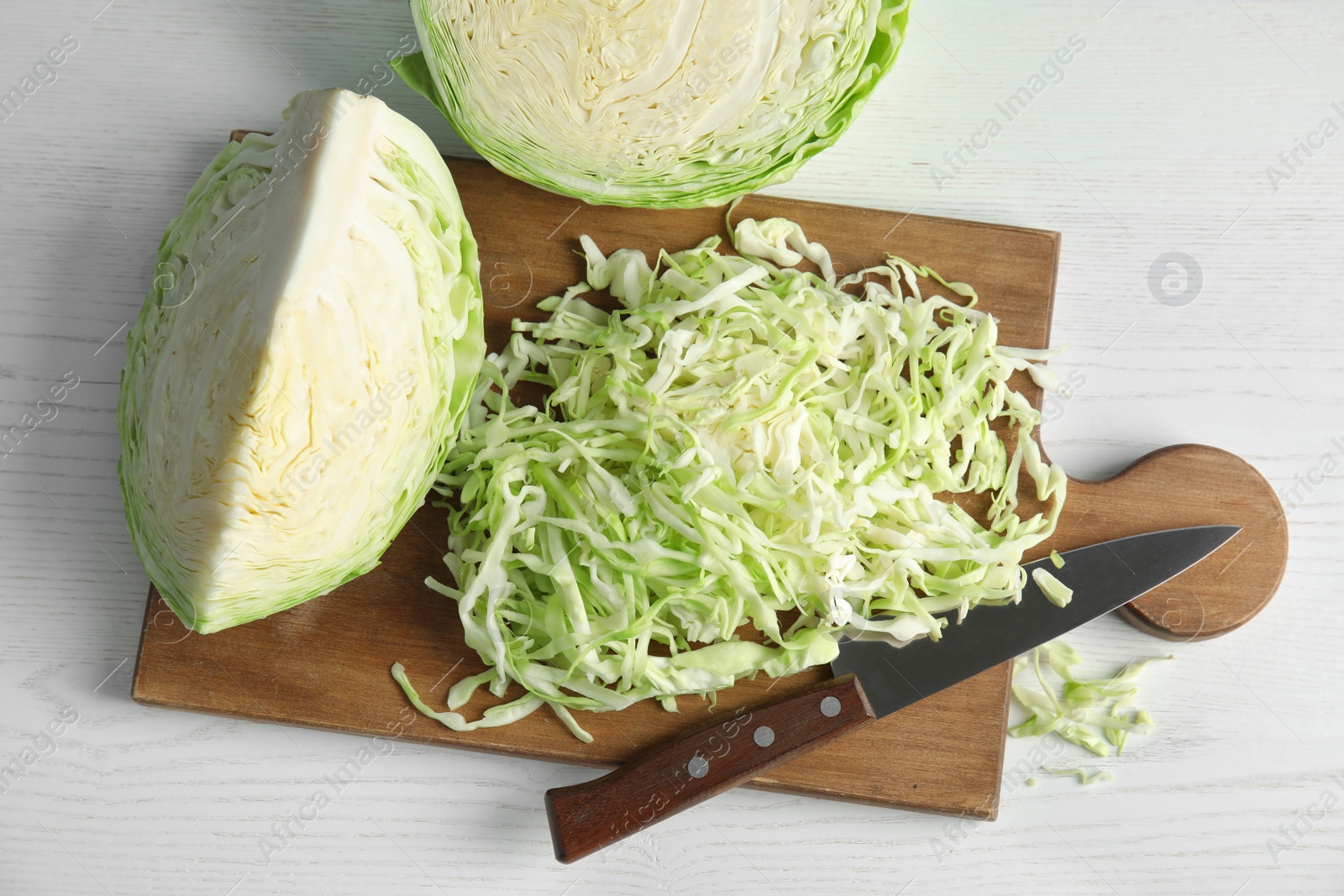 Photo of Cutting board with chopped and sliced cabbage on table