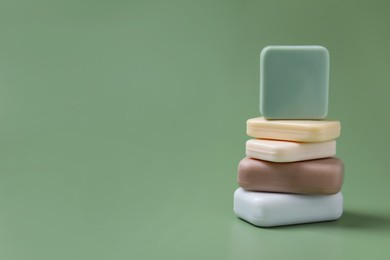 Photo of Many different soap bars stacked on green background, space for text