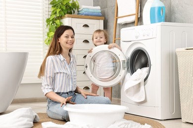 Happy mother with her daughter having fun while washing baby clothes in bathroom