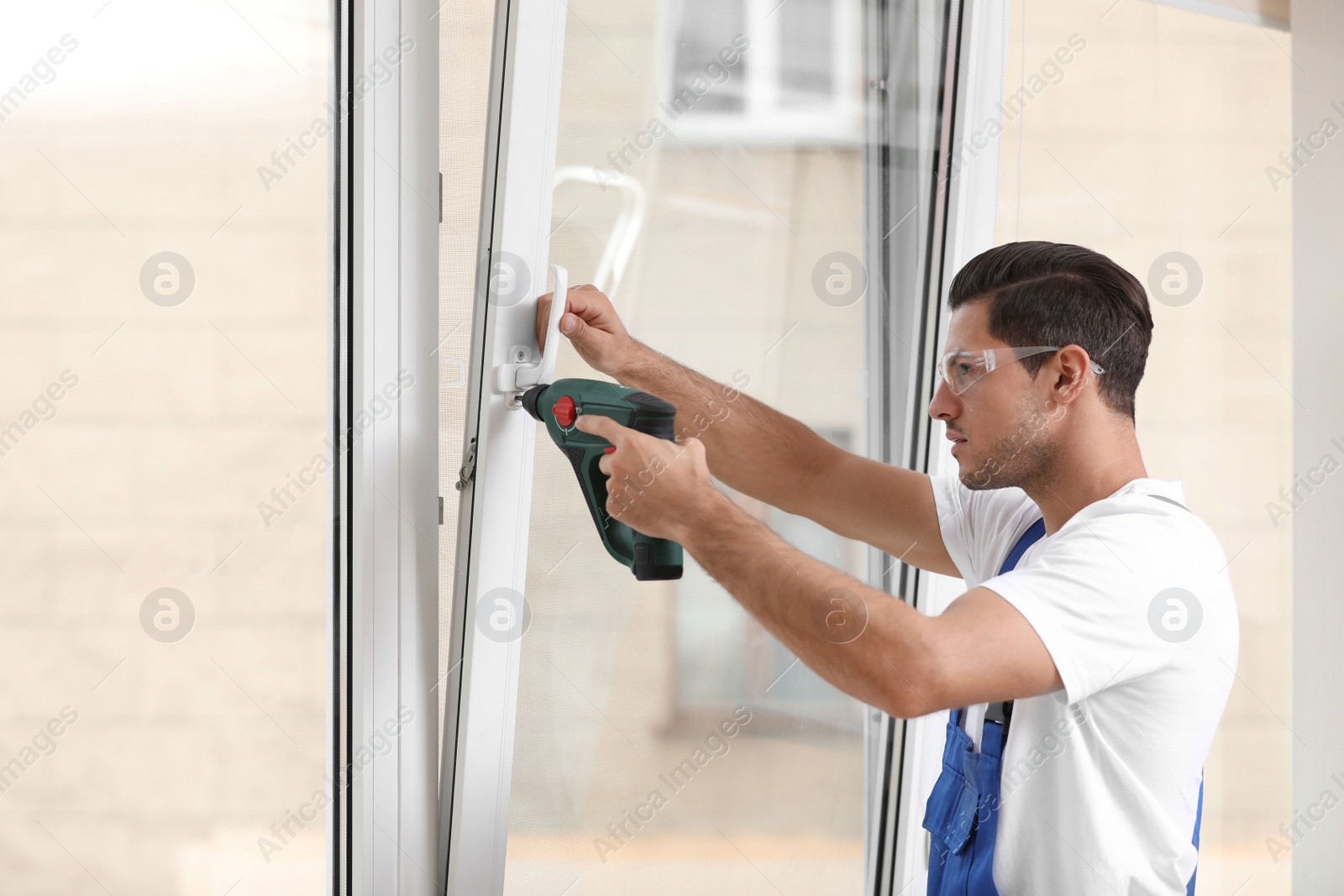 Photo of Construction worker repairing plastic window with electric screwdriver indoors