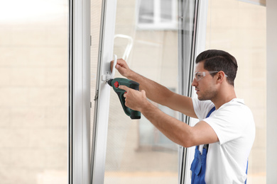 Construction worker repairing plastic window with electric screwdriver indoors