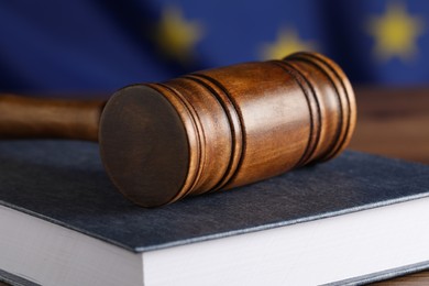 Judge's gavel and book on wooden table against European Union flag, closeup