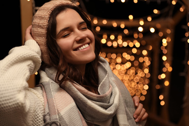 Photo of Young woman wearing warm sweater, hat and scarf  outdoors at night. Winter season