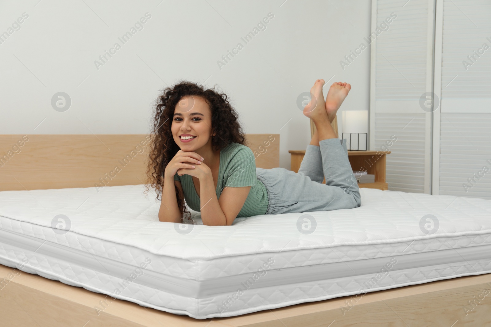 Photo of Happy young African American woman on bed with comfortable mattress at home