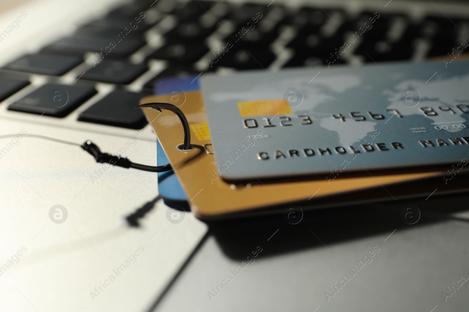 Photo of Fishing hook with credit cards on laptop, closeup. Cyber crime