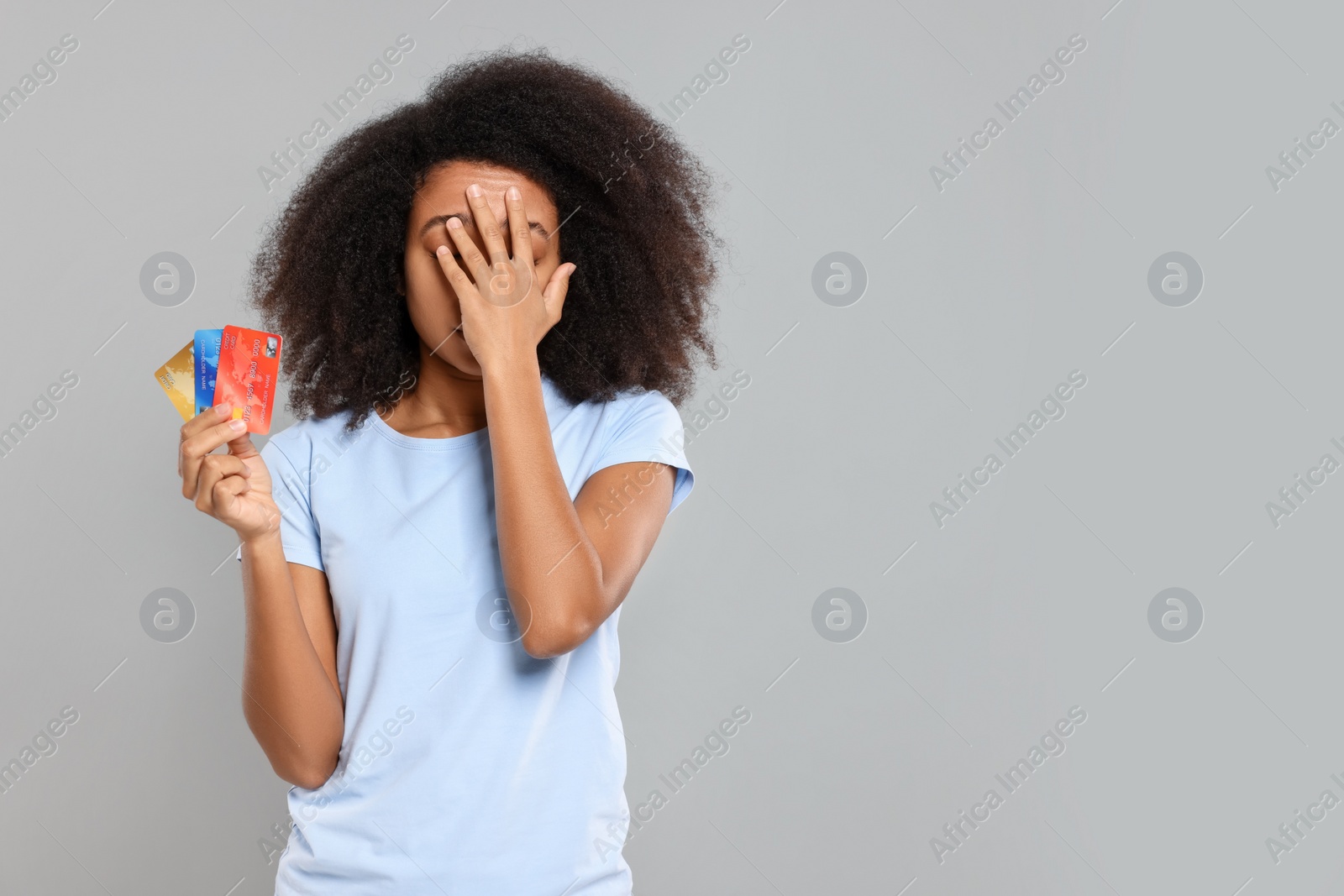 Photo of Confused woman with credit cards on grey background, space for text. Debt problem