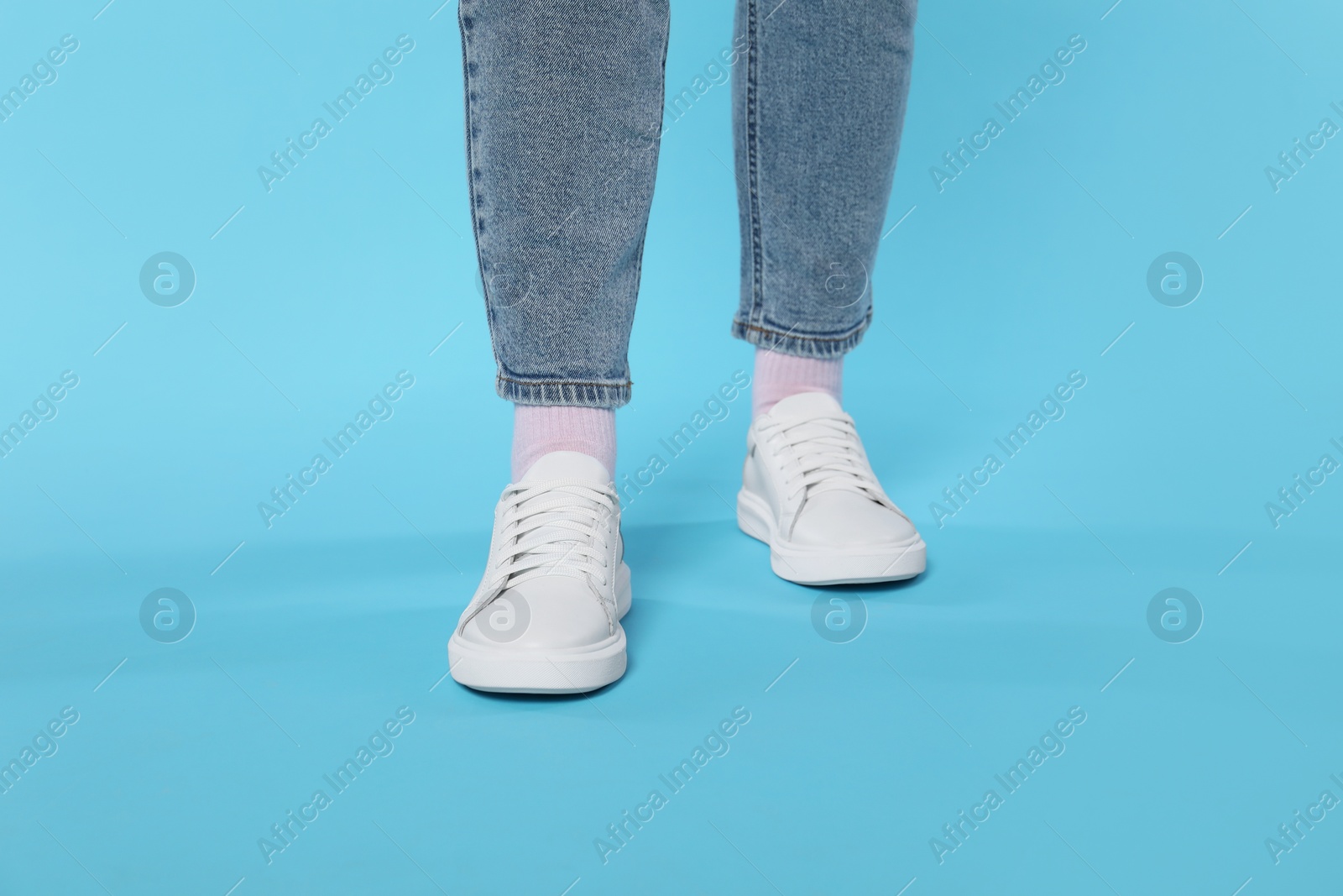 Photo of Woman wearing stylish white sneakers on light blue background, closeup