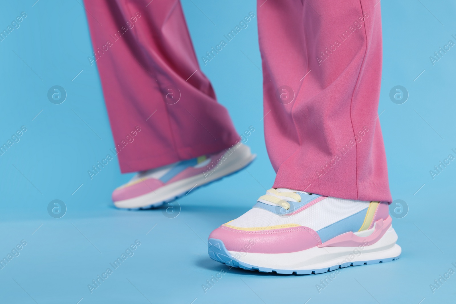 Photo of Woman wearing pair of new stylish sneakers on light blue background, closeup