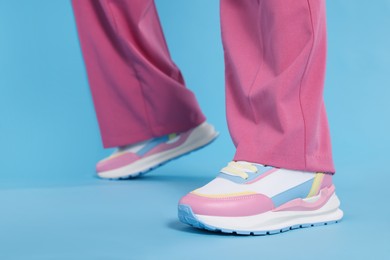 Photo of Woman wearing pairnew stylish sneakers on light blue background, closeup