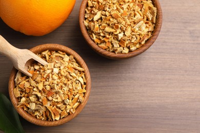 Photo of Bowls of dried orange zest seasoning and fresh fruit on wooden table, flat lay. Space for text
