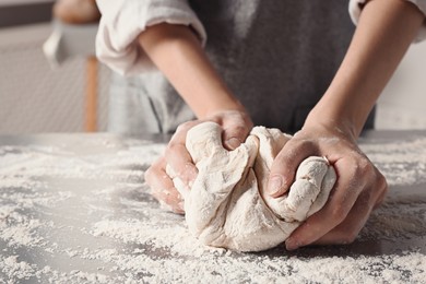 Photo of Woman kneading dough at table in kitchen, closeup