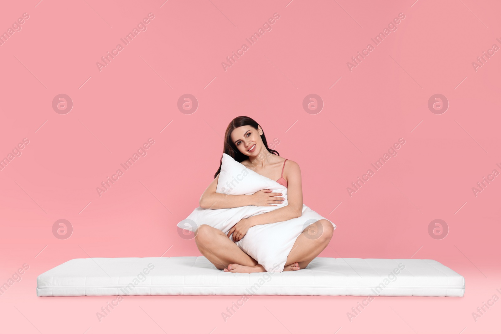 Photo of Young woman on soft mattress holding pillow against pale pink background
