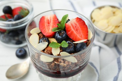 Photo of Tasty granola with berries, jam and almond flakes in glass on white table, closeup