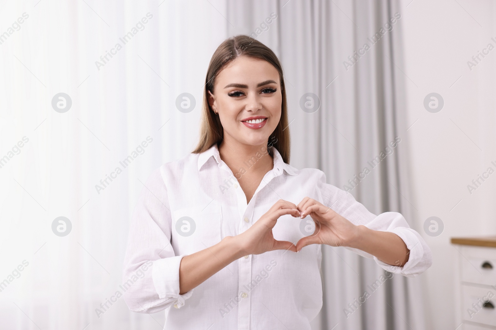 Photo of Happy woman showing heart gesture with hands indoors