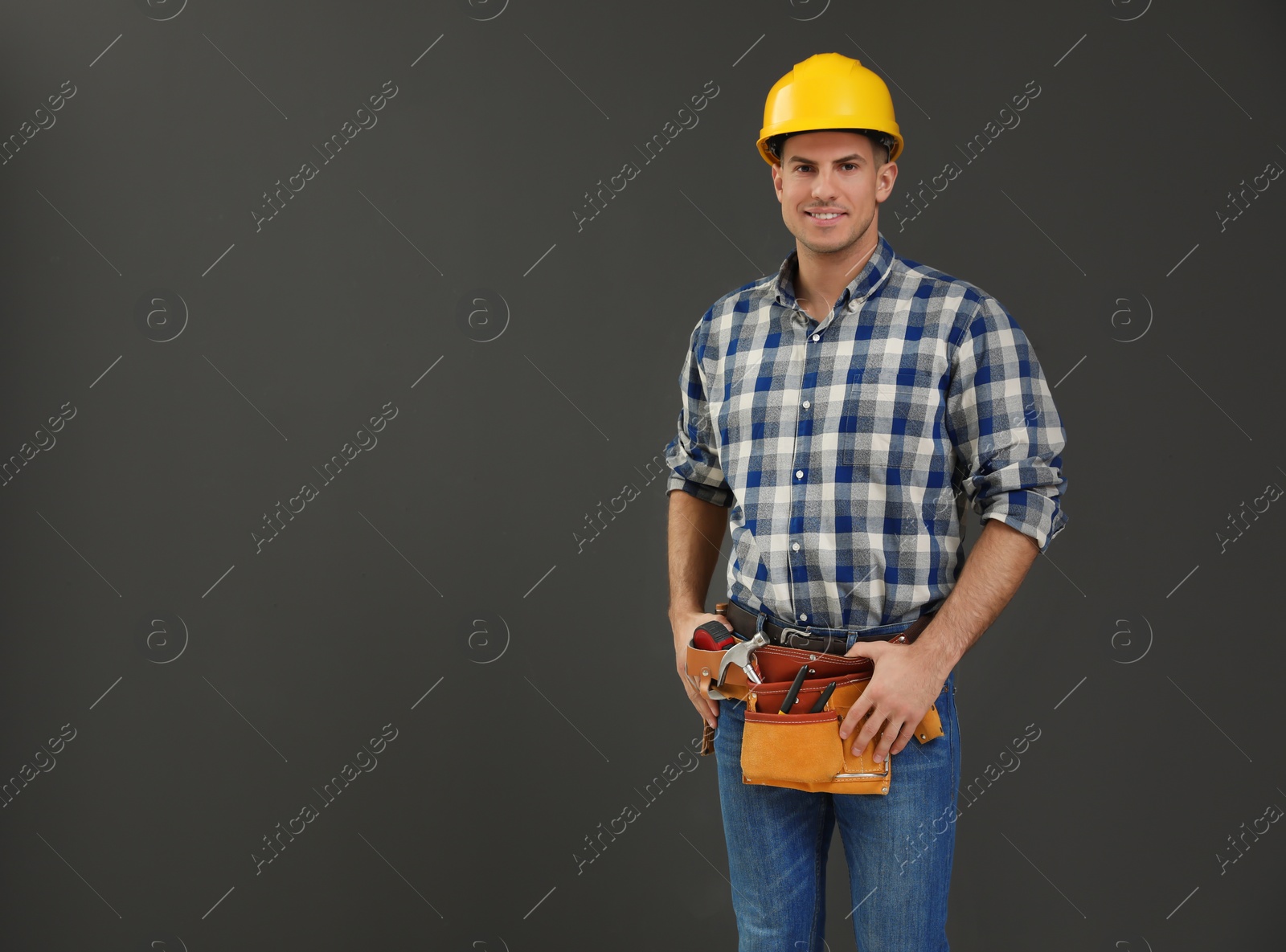 Photo of Handsome carpenter with tool belt on dark background. Space for text