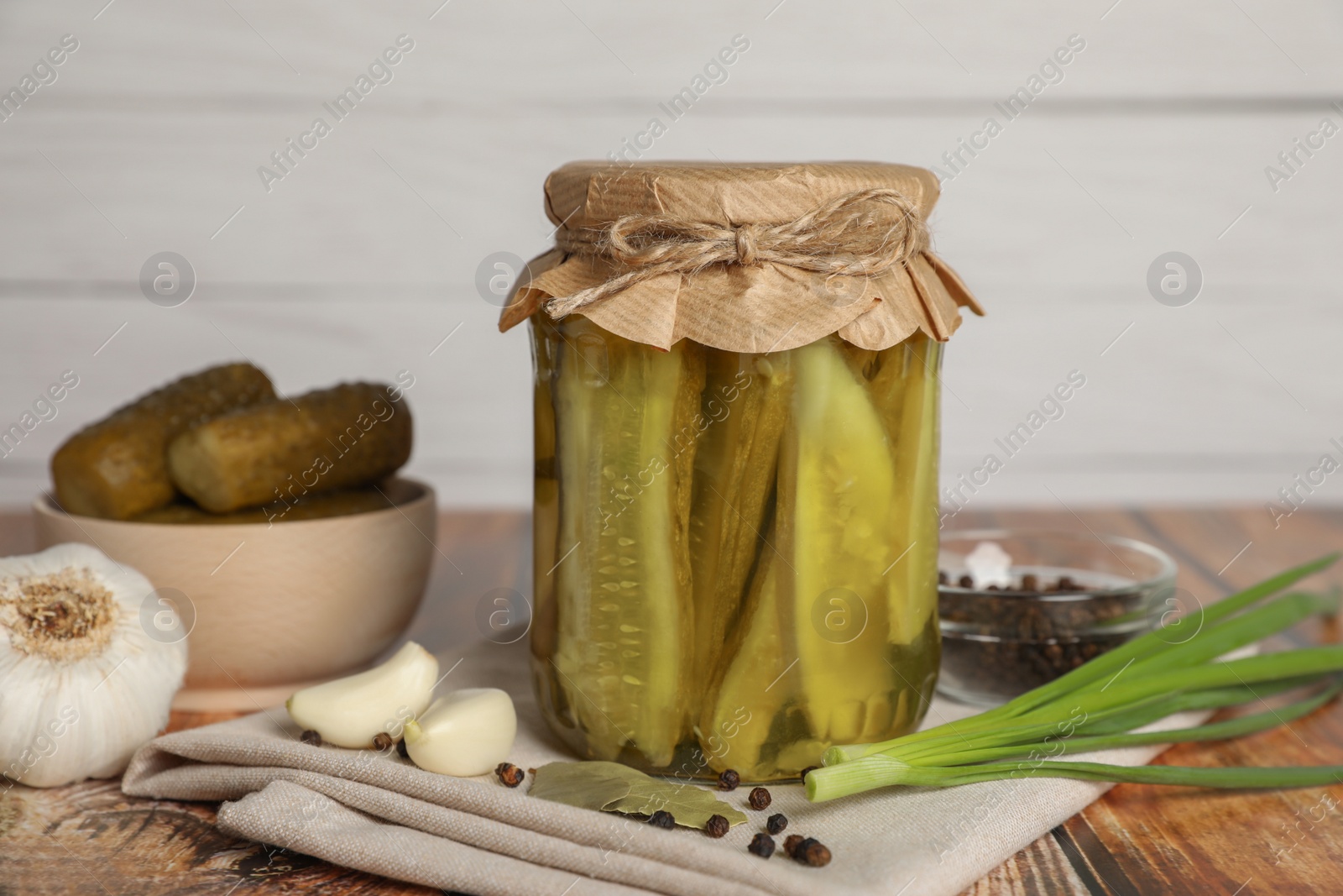Photo of Jar of pickled cucumbers, fresh green onion, peppercorns and garlic on wooden table