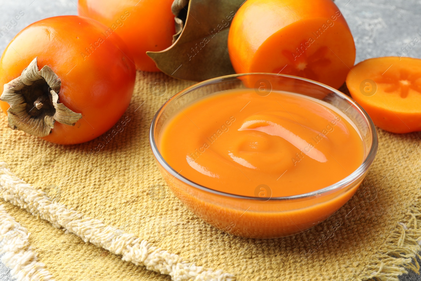 Photo of Delicious persimmon jam in glass bowl and fresh fruits on table