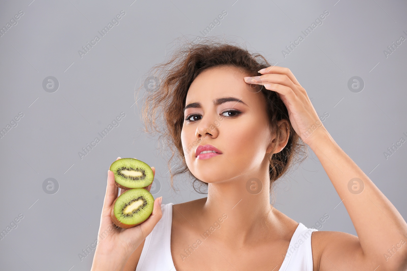 Photo of Beautiful young woman with acne problem holding kiwi on grey background. Skin allergy