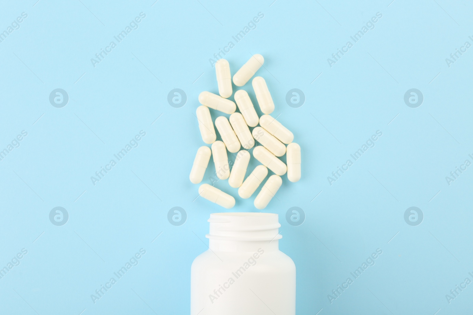 Photo of Bottle and vitamin capsules on light blue background, top view