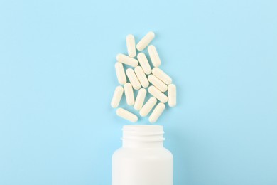 Bottle and vitamin capsules on light blue background, top view