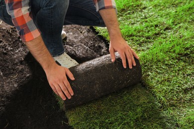 Photo of Young man laying grass sod on ground at backyard, closeup