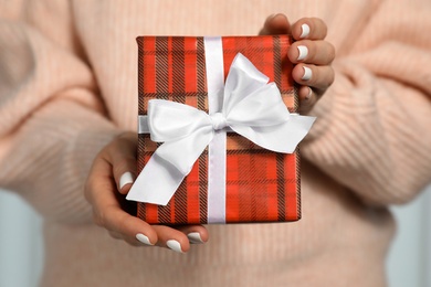 Photo of Woman in warm sweater holding Christmas gift on light background, closeup