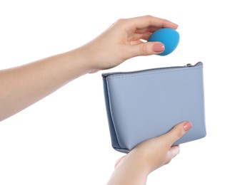 Woman putting makeup sponge into cosmetic bag on white background, closeup