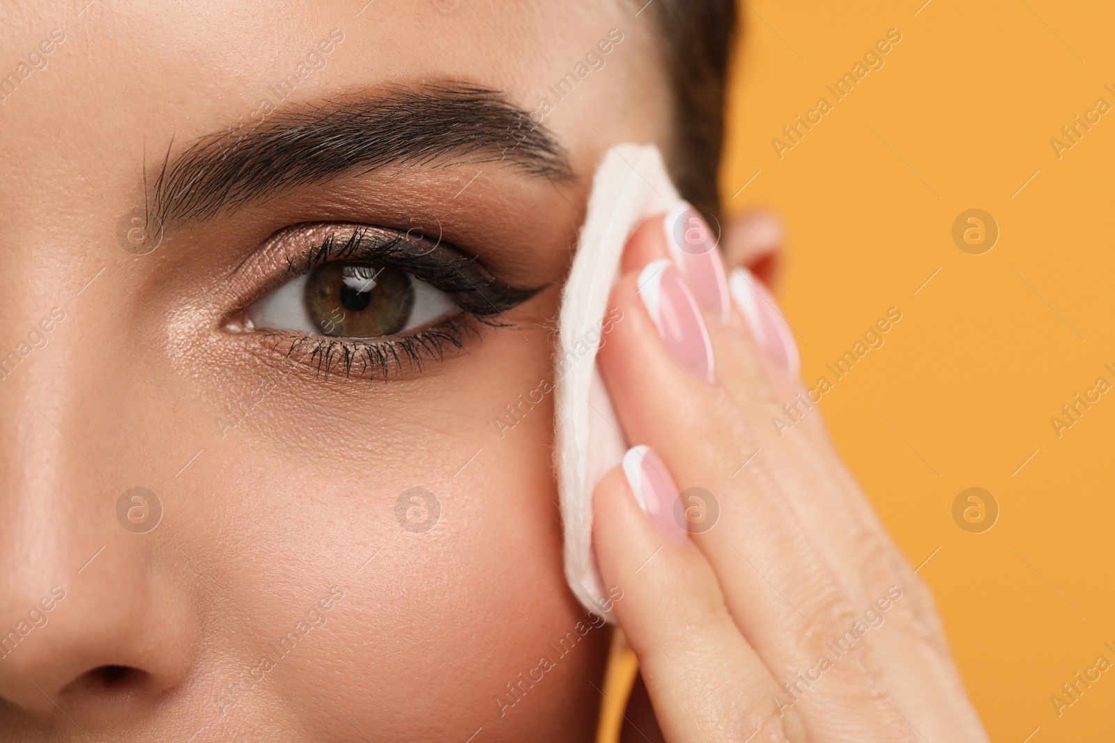 Photo of Beautiful woman removing makeup with cotton pad on orange background, closeup. Space for text