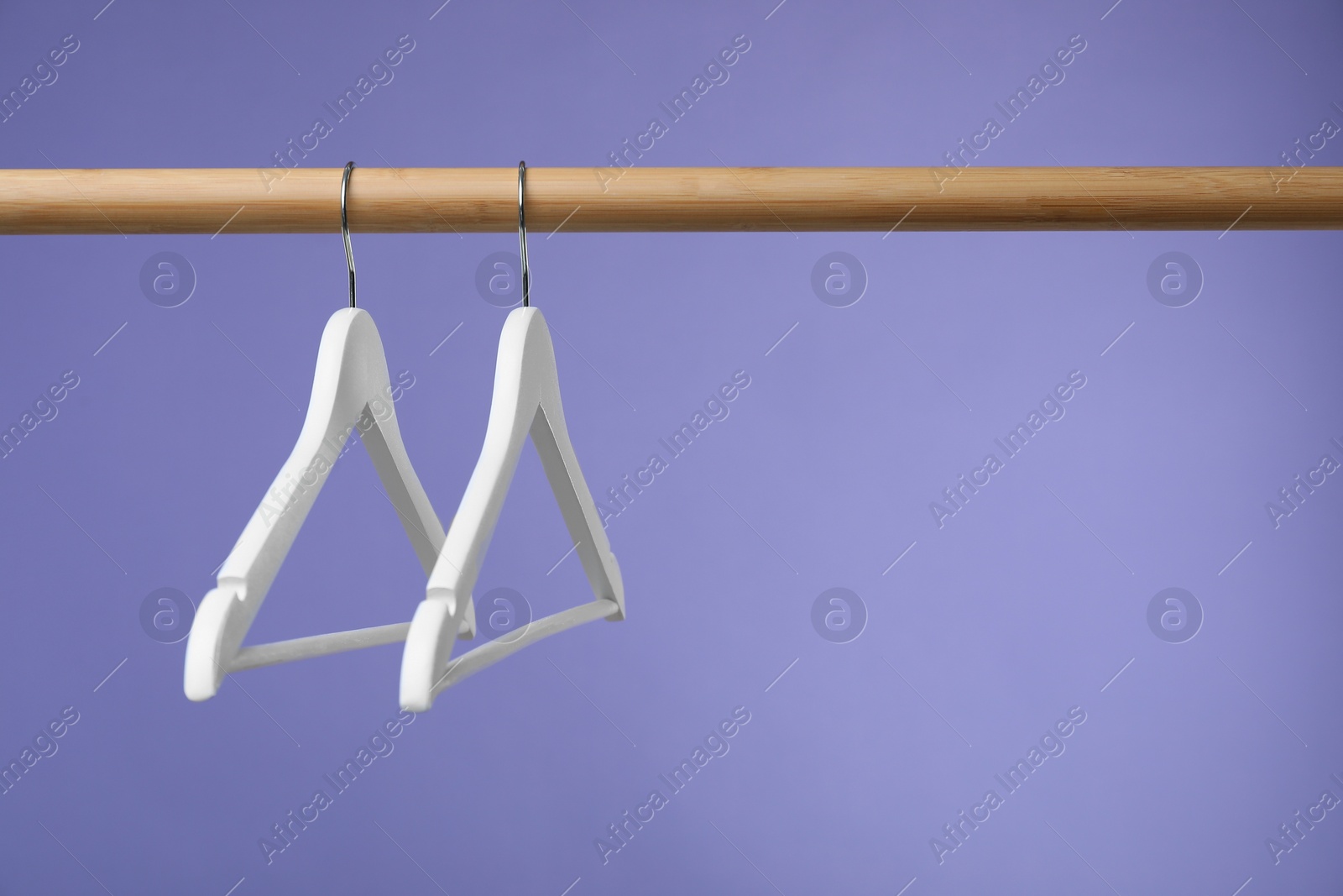 Photo of Empty clothes hangers on wooden rack against purple background. Space for text