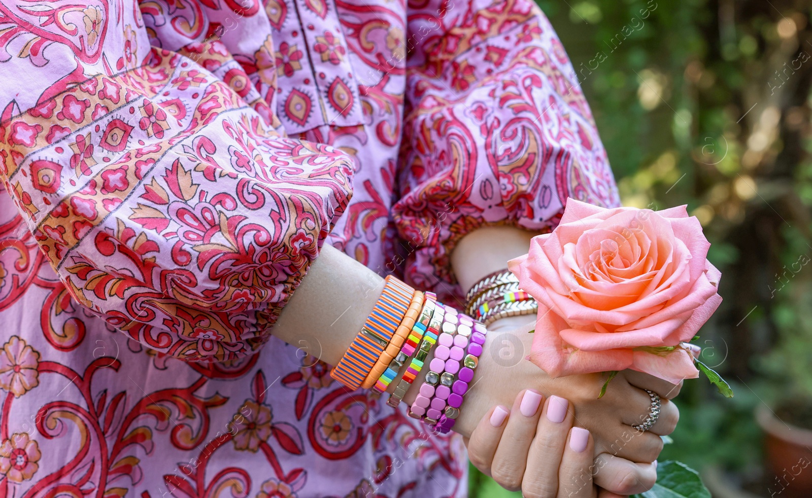 Photo of Woman wearing bracelets and holding pink rose outdoors, closeup