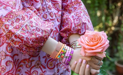 Photo of Woman wearing bracelets and holding pink rose outdoors, closeup