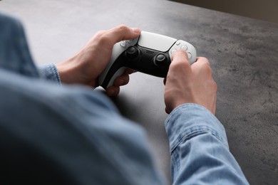 Photo of Man using wireless game controller at grey table, closeup