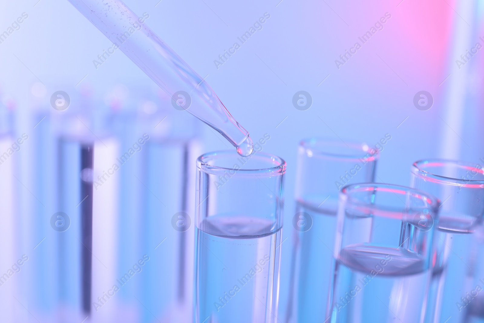 Photo of Dripping liquid from pipette into test tube on color background, closeup