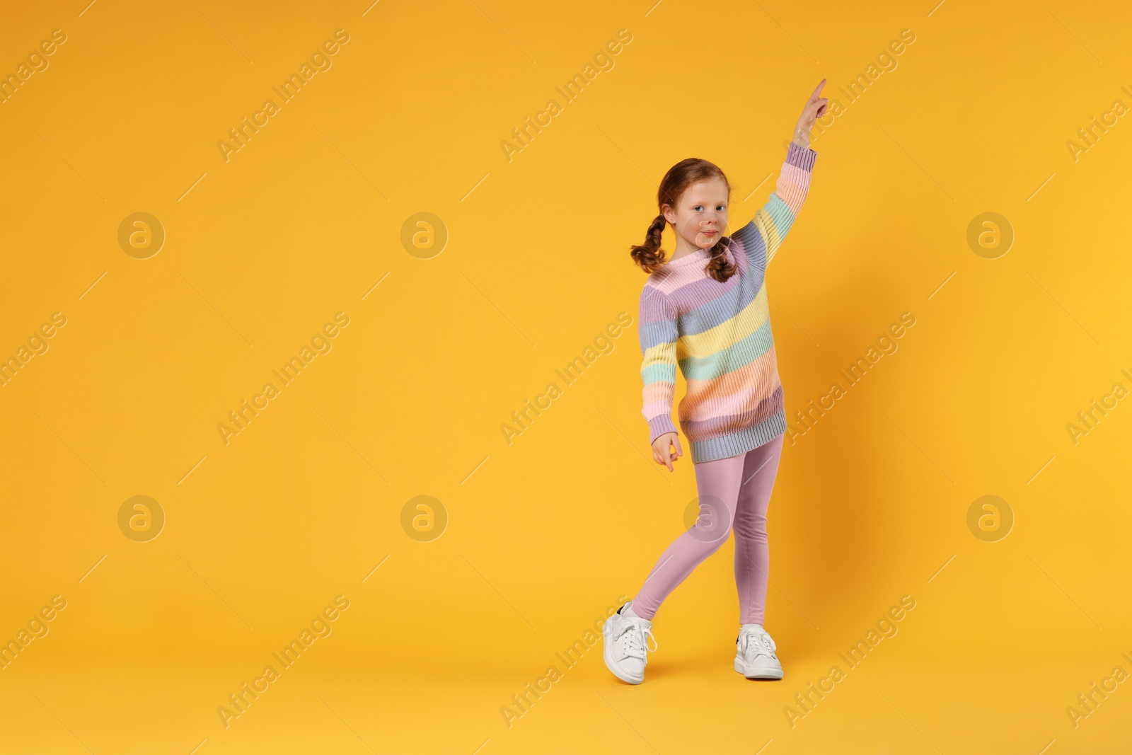 Photo of Cute little girl dancing on orange background, space for text