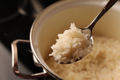 Wooden spoon with delicious rice over pot, closeup