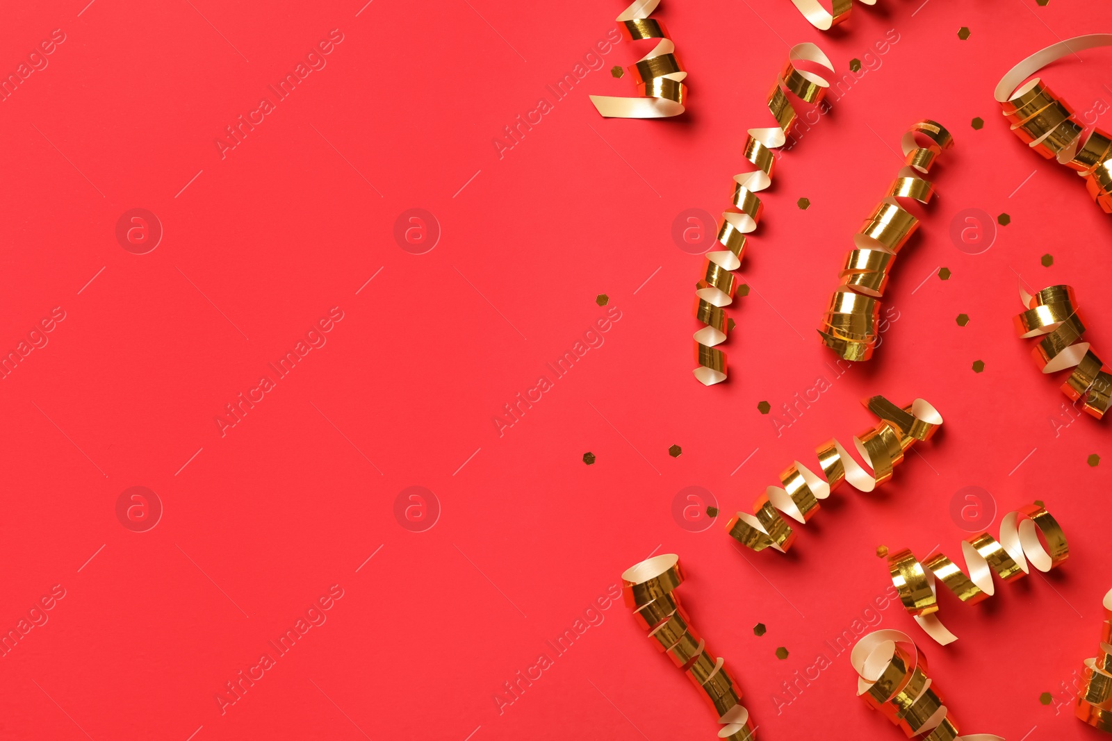 Photo of Shiny golden serpentine streamers and confetti on red background, flat lay. Space for text