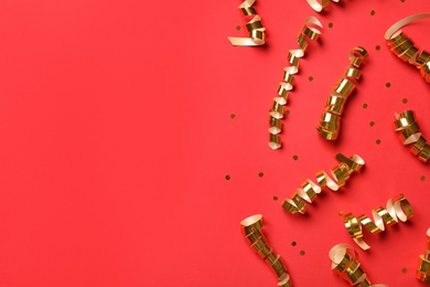 Photo of Shiny golden serpentine streamers and confetti on red background, flat lay. Space for text