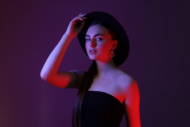 Photo of Portrait of beautiful young woman in hat on color background with neon lights