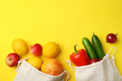 Cotton eco bags with fruits and vegetables on yellow background, flat lay. Space for text