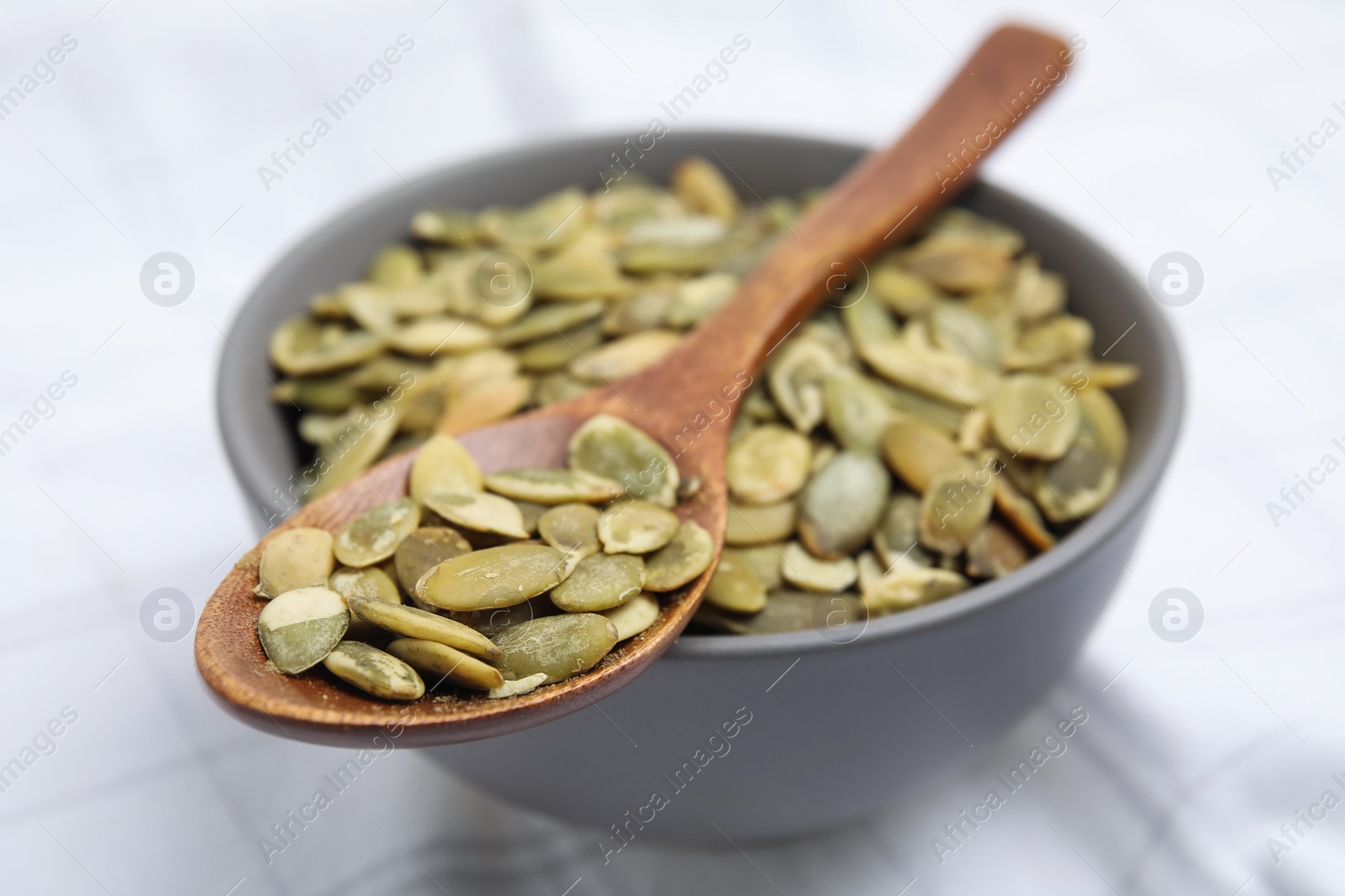 Photo of Bowl with pumpkin seeds and wooden spoon on tablecloth, closeup