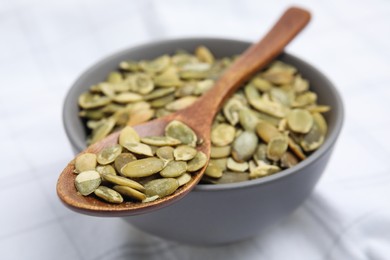 Photo of Bowl with pumpkin seeds and wooden spoon on tablecloth, closeup